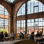 Home 22 폐공간 활용을 위한 지역 발전 전략 - A wide-angle, vibrant interior shot of a transformed abandoned industrial factory, now a thriving cu...